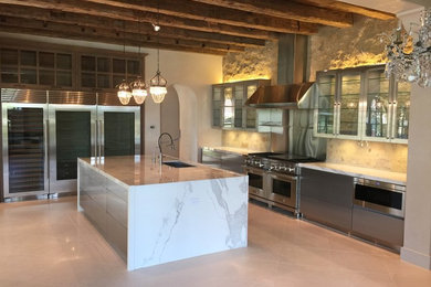 Example of a mid-sized trendy single-wall marble floor eat-in kitchen design in Houston with a double-bowl sink, flat-panel cabinets, stainless steel cabinets, marble countertops, beige backsplash, stone tile backsplash, stainless steel appliances and an island