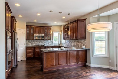Inspiration for a large timeless u-shaped dark wood floor eat-in kitchen remodel in Indianapolis with an undermount sink, raised-panel cabinets, medium tone wood cabinets, granite countertops, gray backsplash, glass tile backsplash and stainless steel appliances