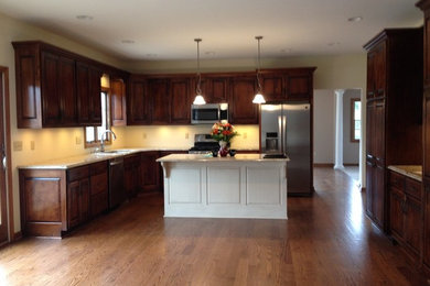 Mid-sized l-shaped medium tone wood floor open concept kitchen photo in Cleveland with an undermount sink, raised-panel cabinets, dark wood cabinets, granite countertops, stainless steel appliances and an island