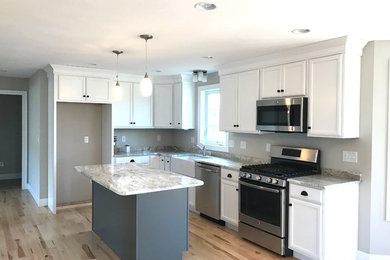 Photo of a medium sized classic l-shaped kitchen/diner in Boston with a belfast sink, flat-panel cabinets, white cabinets, granite worktops, stainless steel appliances, light hardwood flooring, an island and multi-coloured floors.