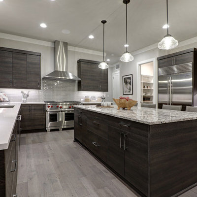 Example of a large minimalist u-shaped medium tone wood floor and gray floor enclosed kitchen design in Chicago with flat-panel cabinets, dark wood cabinets, gray backsplash, glass tile backsplash, stainless steel appliances, an island and an undermount sink
