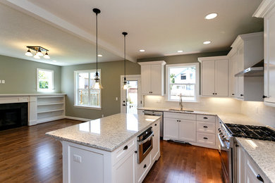 Exempel på ett mellanstort amerikanskt flerfärgad flerfärgat kök, med en undermonterad diskho, luckor med infälld panel, vita skåp, granitbänkskiva, vitt stänkskydd, stänkskydd i tunnelbanekakel, rostfria vitvaror, mellanmörkt trägolv, en köksö och brunt golv