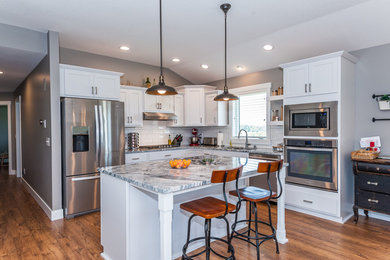 Example of a mid-sized country l-shaped dark wood floor and brown floor open concept kitchen design in Other with shaker cabinets, white cabinets, granite countertops, white backsplash, subway tile backsplash, stainless steel appliances and an island