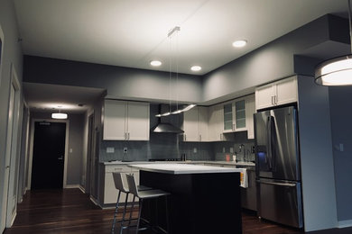 Foto på ett avskilt, mellanstort funkis vit l-kök, med skåp i shakerstil, vita skåp, träbänkskiva, grått stänkskydd, rostfria vitvaror, mörkt trägolv, en köksö och brunt golv