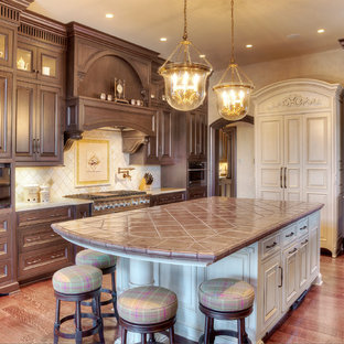 This is an example of a large traditional l-shaped eat-in kitchen in Kansas City with raised-panel cabinets, brown cabinets, tile benchtops, white splashback, ceramic splashback, stainless steel appliances and with island.