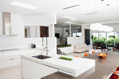 Large contemporary l-shaped open plan kitchen in New York with a submerged sink, flat-panel cabinets, white cabinets, composite countertops, stainless steel appliances, limestone flooring, an island and beige floors.