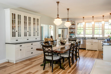 Eat-in kitchen - large farmhouse u-shaped light wood floor eat-in kitchen idea in New York with a farmhouse sink, white cabinets, granite countertops, ceramic backsplash, white appliances, no island and black countertops