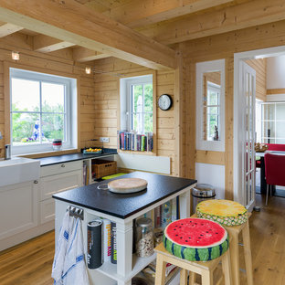 Geschlossene Landhaus Küche mit Landhausspüle, Schrankfronten im Shaker-Stil, weißen Schränken, hellem Holzboden, Kücheninsel, Küchenrückwand in Braun, Rückwand aus Holz und braunem Boden in Köln