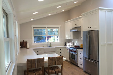 Mid-sized farmhouse u-shaped light wood floor eat-in kitchen photo in San Francisco with a farmhouse sink, shaker cabinets, white cabinets, quartzite countertops, white backsplash, ceramic backsplash, stainless steel appliances and a peninsula