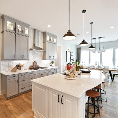 Urban light wood floor and beige floor kitchen photo in Charlotte with gray cabinets, quartz countertops, white backsplash, subway tile backsplash, stainless steel appliances, an island and white countertops