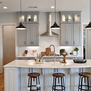 Example of a transitional l-shaped medium tone wood floor and brown floor kitchen design in Charlotte with an undermount sink, shaker cabinets, gray cabinets, white backsplash, subway tile backsplash, stainless steel appliances, an island and white countertops