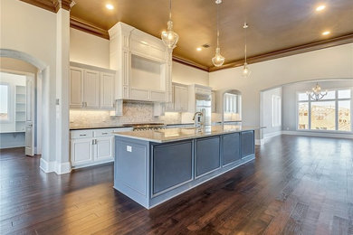 Large trendy single-wall medium tone wood floor open concept kitchen photo in Dallas with an undermount sink, recessed-panel cabinets, white cabinets, white backsplash, ceramic backsplash, stainless steel appliances and an island