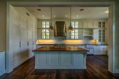 Cette image montre une cuisine traditionnelle avec un placard avec porte à panneau encastré, des portes de placard blanches, une crédence en céramique, un électroménager en acier inoxydable, un sol en bois brun et îlot.