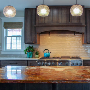 Imagen de cocina comedor en U, tradicional renovada, grande, con fregadero bajoencimera, armarios estilo shaker, encimera de ónix, salpicadero beige, salpicadero de azulejos de cerámica, electrodomésticos de acero inoxidable, suelo de madera clara, una isla, suelo beige, encimeras naranjas y puertas de armario de madera oscura