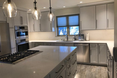 Mid-sized transitional u-shaped porcelain tile and gray floor eat-in kitchen photo in Denver with a single-bowl sink, recessed-panel cabinets, white cabinets, quartz countertops, white backsplash, stainless steel appliances, an island and white countertops