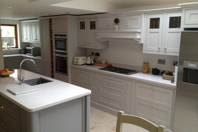 Photo of a medium sized modern l-shaped kitchen/diner in Dublin with a single-bowl sink, beaded cabinets, grey cabinets, quartz worktops, white splashback, stone slab splashback, stainless steel appliances, travertine flooring and an island.