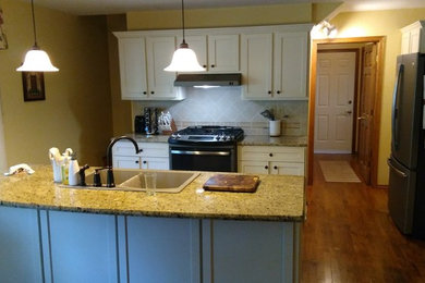 Eat-in kitchen - large traditional u-shaped medium tone wood floor and brown floor eat-in kitchen idea in Grand Rapids with a drop-in sink, shaker cabinets, white cabinets, white backsplash, stainless steel appliances and an island