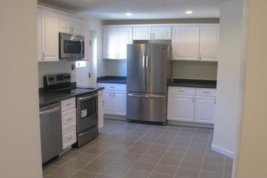 Mid-sized minimalist l-shaped ceramic tile enclosed kitchen photo in Boston with a drop-in sink, flat-panel cabinets, white cabinets, granite countertops, white backsplash, porcelain backsplash, stainless steel appliances and no island