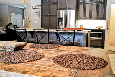 Example of a mid-sized mountain style l-shaped medium tone wood floor and brown floor eat-in kitchen design in Other with a double-bowl sink, recessed-panel cabinets, dark wood cabinets, granite countertops, stainless steel appliances, an island and gray countertops