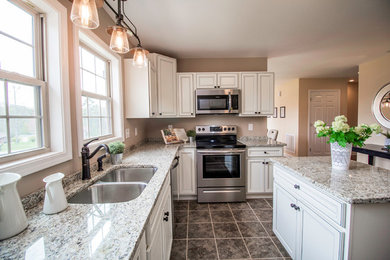 Mid-sized transitional u-shaped ceramic tile and brown floor enclosed kitchen photo in Charlotte with a double-bowl sink, raised-panel cabinets, white cabinets, granite countertops, stainless steel appliances, an island and gray countertops