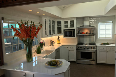 Example of a large transitional u-shaped brown floor kitchen design in Orange County with a farmhouse sink, shaker cabinets, white cabinets, solid surface countertops, white backsplash, subway tile backsplash, stainless steel appliances, no island and white countertops