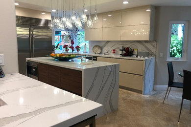 Large trendy u-shaped porcelain tile and beige floor kitchen photo in Orange County with an undermount sink, flat-panel cabinets, beige cabinets, quartzite countertops, white backsplash, stone slab backsplash, stainless steel appliances, an island and white countertops
