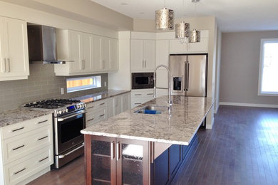 Kitchen - contemporary l-shaped dark wood floor and brown floor kitchen idea in Calgary with a double-bowl sink, shaker cabinets, white cabinets, granite countertops, green backsplash, glass tile backsplash, stainless steel appliances and an island