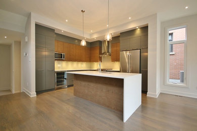Example of a mid-sized trendy l-shaped light wood floor eat-in kitchen design in Ottawa with a double-bowl sink, flat-panel cabinets, gray cabinets, quartz countertops, gray backsplash, glass tile backsplash, stainless steel appliances and an island