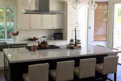サンディエゴにある広いトランジショナルスタイルのおしゃれなキッチン (エプロンフロントシンク、シェーカースタイル扉のキャビネット、白いキャビネット、白いキッチンパネル、サブウェイタイルのキッチンパネル、シルバーの調理設備、濃色無垢フローリング、茶色い床、御影石カウンター) の写真