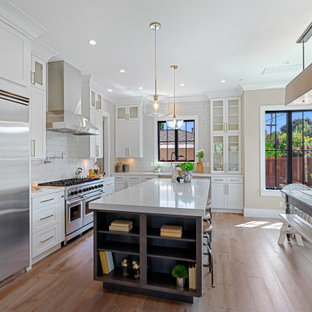 Mid-sized farmhouse eat-in kitchen designs - Eat-in kitchen - mid-sized farmhouse u-shaped medium tone wood floor and brown floor eat-in kitchen idea in San Francisco with a farmhouse sink, white cabinets, quartz countertops, gray backsplash, ceramic backsplash, stainless steel appliances, an island, white countertops and recessed-panel cabinets