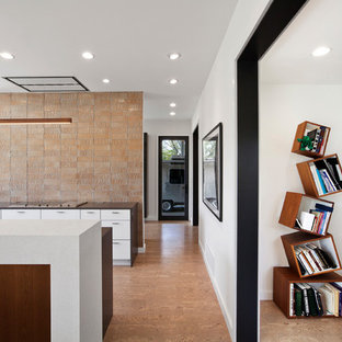 Modelo de cocina comedor en L, moderna, de tamaño medio, con fregadero bajoencimera, armarios con paneles lisos, puertas de armario blancas, encimera de cuarzo compacto, salpicadero naranja, salpicadero de azulejos de vidrio, electrodomésticos de acero inoxidable, suelo de corcho, una isla y suelo beige