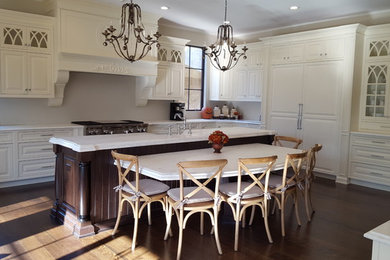 Eat-in kitchen - large mediterranean u-shaped dark wood floor and brown floor eat-in kitchen idea in New York with a farmhouse sink, raised-panel cabinets, white cabinets, marble countertops, white backsplash, stone slab backsplash, paneled appliances, an island and white countertops