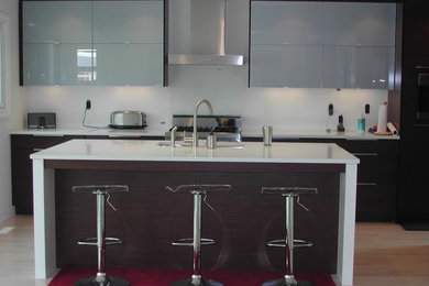 Example of a mid-sized minimalist single-wall light wood floor open concept kitchen design in Calgary with an undermount sink, flat-panel cabinets, dark wood cabinets, quartz countertops, white backsplash, stainless steel appliances and an island