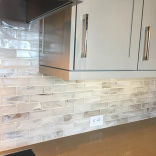 Design ideas for a large industrial l-shaped open plan kitchen in Atlanta with a farmhouse sink, shaker cabinets, grey cabinets, recycled glass benchtops, white splashback, glass tile splashback, stainless steel appliances, with island and beige floor.
