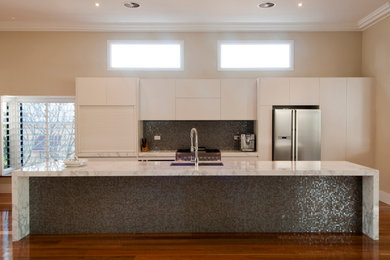 Inredning av ett modernt kök, med en undermonterad diskho, släta luckor, vita skåp, marmorbänkskiva, flerfärgad stänkskydd, stänkskydd i mosaik, rostfria vitvaror, mellanmörkt trägolv och en köksö