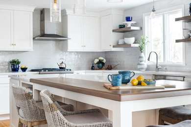 Nautical l-shaped kitchen/diner in Boston with white cabinets, white splashback, stainless steel appliances, medium hardwood flooring, an island, brown floors and white worktops.