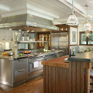 Idée de décoration pour une très grand cuisine américaine victorienne avec un placard à porte affleurante, une façade en inox, une crédence métallisée, un électroménager en acier inoxydable, un évier posé, une crédence en dalle métallique, un sol en bois brun, 2 îlots et un plan de travail en inox.