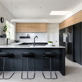 This is an example of a contemporary u-shaped kitchen in Hobart with flat-panel cabinets, black cabinets, white splashback, black appliances, a peninsula, beige floor and white benchtop.