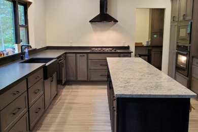 Mid-sized transitional porcelain tile and gray floor kitchen photo in Other with a farmhouse sink, shaker cabinets, gray cabinets, quartz countertops, black backsplash, stone slab backsplash, stainless steel appliances, an island and white countertops