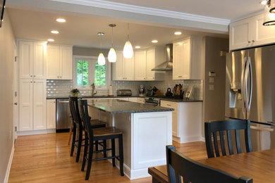 Example of a large classic medium tone wood floor and brown floor eat-in kitchen design in Bridgeport with a single-bowl sink, shaker cabinets, white cabinets, granite countertops, white backsplash, ceramic backsplash, stainless steel appliances, an island and black countertops