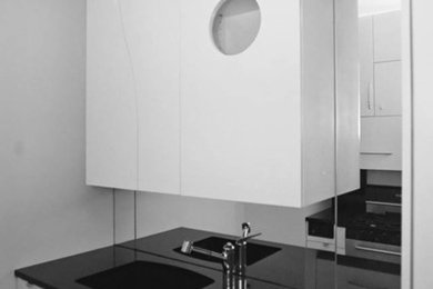 Foto på ett litet funkis kök, med en undermonterad diskho, släta luckor, vita skåp, granitbänkskiva, glaspanel som stänkskydd, vita vitvaror och en halv köksö