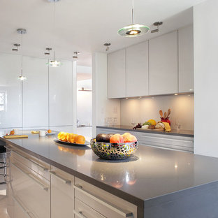 Mid-sized modern eat-in kitchen in New York with quartz benchtops, grey splashback, glass sheet splashback, stainless steel appliances, an undermount sink, flat-panel cabinets, stainless steel cabinets, porcelain floors and with island.