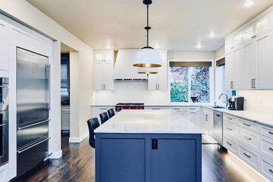 Mid-sized elegant l-shaped dark wood floor and brown floor enclosed kitchen photo in Seattle with an undermount sink, shaker cabinets, white cabinets, quartzite countertops, white backsplash, ceramic backsplash, stainless steel appliances, an island and white countertops