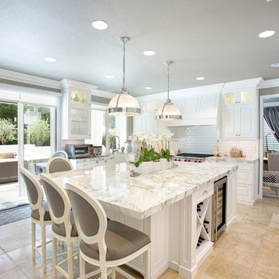 Eat-in kitchen - large transitional l-shaped travertine floor and beige floor eat-in kitchen idea with a farmhouse sink, raised-panel cabinets, white cabinets, marble countertops, white backsplash, subway tile backsplash, stainless steel appliances and an island