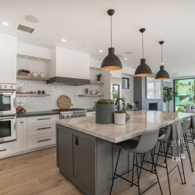 Example of a trendy l-shaped medium tone wood floor and brown floor kitchen design in Orange County with shaker cabinets, white cabinets, gray backsplash, stainless steel appliances, an island and gray countertops