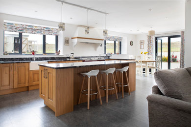 Inspiration for a country galley open plan kitchen in Cornwall with a belfast sink, raised-panel cabinets, medium wood cabinets, an island, grey floors and black worktops.
