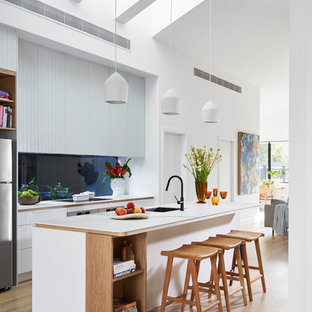 Contemporary open plan kitchen in Melbourne with a single-bowl sink, white cabinets, blue splashback, glass sheet splashback, stainless steel appliances, light hardwood floors, with island, beige floor and white benchtop.