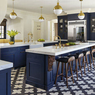 Ejemplo de cocina comedor de galera, clásica renovada, con puertas de armario azules, electrodomésticos de acero inoxidable, suelo de baldosas de cerámica, dos o más islas, suelo negro, encimeras blancas, fregadero bajoencimera, armarios con rebordes decorativos, salpicadero blanco y salpicadero de piedra caliza