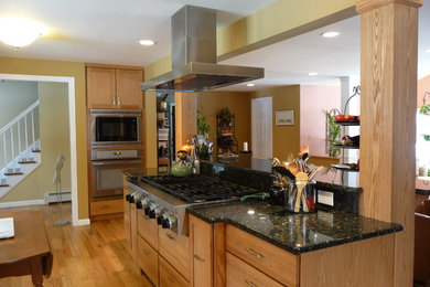 Imagen de cocina contemporánea con puertas de armario de madera clara, salpicadero negro, electrodomésticos de acero inoxidable, suelo de madera clara y una isla