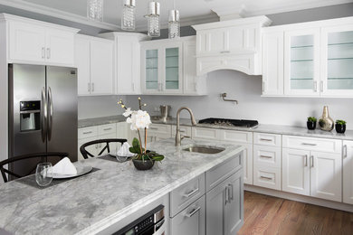 Example of a mid-sized trendy u-shaped medium tone wood floor and brown floor enclosed kitchen design in New York with an undermount sink, recessed-panel cabinets, white cabinets, white backsplash, stainless steel appliances, an island and gray countertops